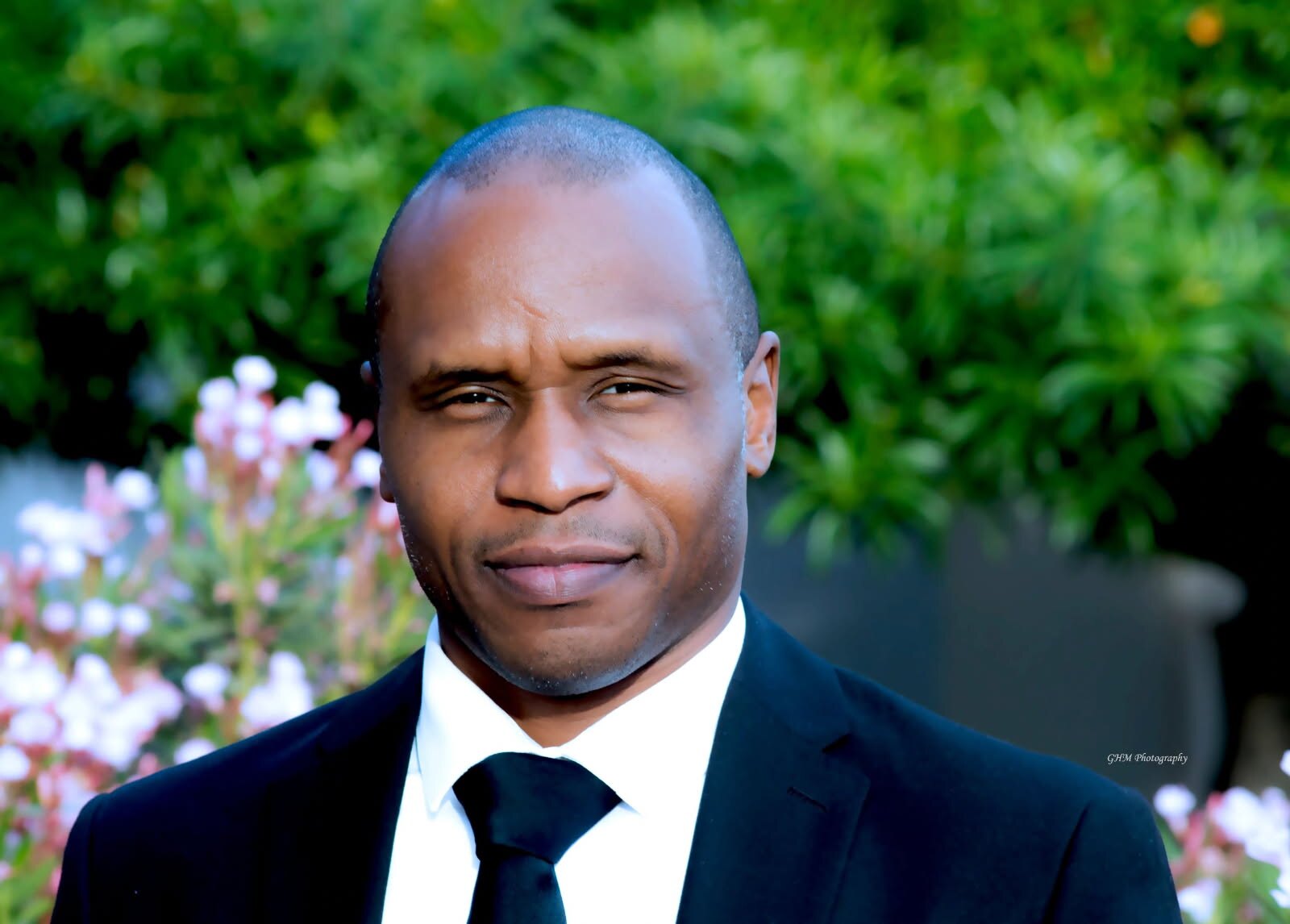 Professional headshot of a man in a dark suit and tie outdoors