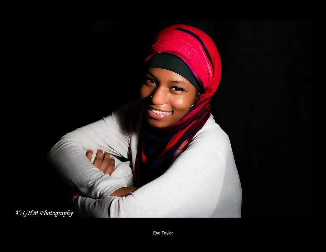 Personal portrait of a woman in a red headwrap against a dark background