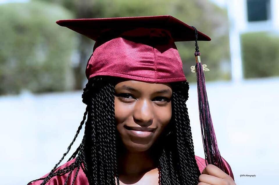 Graduate in a maroon cap and gown smiling outdoors