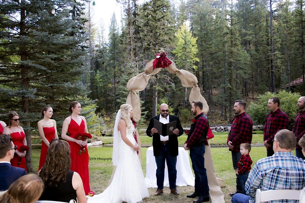 A wedding ceremony taking place beneath a floral arch in the woods