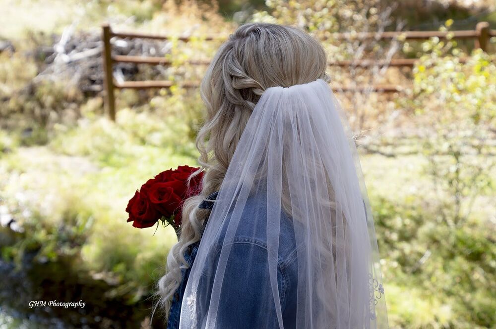A bride in a veil holding red roses and gazing into a wooded landscape